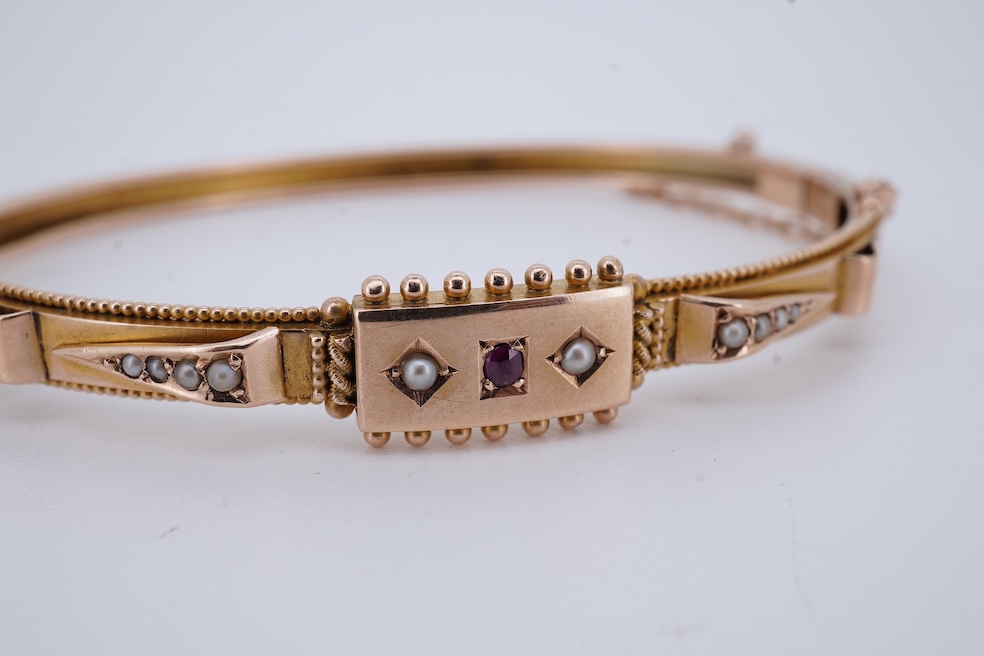 An Edwardian 9ct, seed pearl and ruby set hinged bangle, interior diameter 57mm, gross weight 8.3 grams. Condition - poor to fair